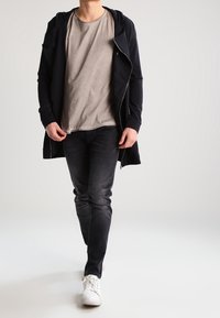 Černá mikina na zip přes světle šedé tričko, doplněná o tmavé džíny a bílé tenisky. Zaměřeno na ležérní, vrstvený outfit.