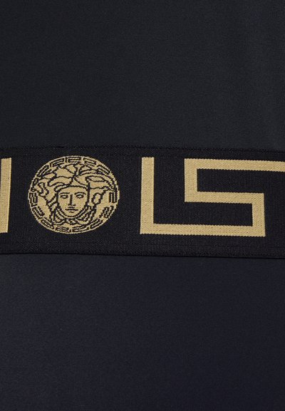 Black fabric with a wide gold logo band featuring a Medusa head and geometric shapes, showcasing a smooth texture and bold design.