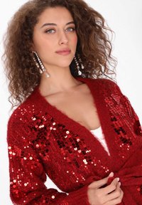 Czerwony kardigan z cekinami, miękka tekstura, otwarty przód, długie rękawy i wiązany detal w talii. Charakteryzuje się blaskiem i głębią dzięki cekinom.