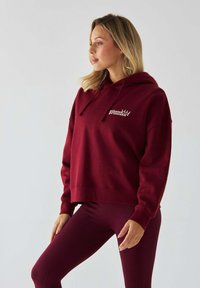 Bordeaux krótka bluza z kapturem, wykonana z miękkiego materiału z troczkami, z białym logo "pilate princess" na piersi. W komplecie ze współpasującymi legginsami.