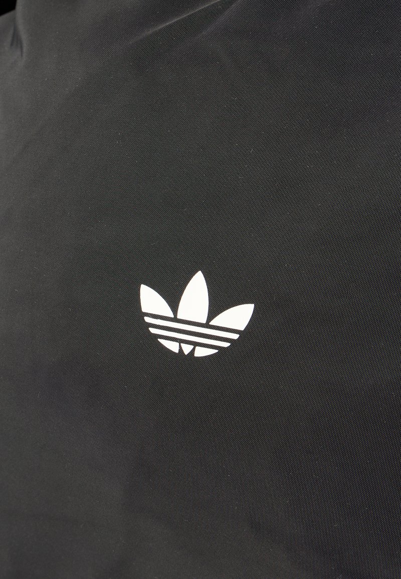 Tela negra con un logotipo blanco de Adidas trefoil con tres rayas horizontales. La textura es lisa y mate.