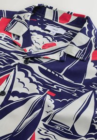 Chemise à manches courtes avec col, motif de voiliers et vagues bleu marine, blanc et rouge, boutonnée devant et étiquette « Next » taille M à l’intérieur du col.
