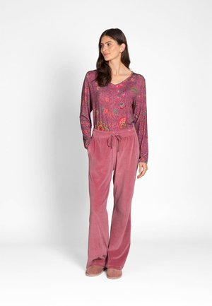 Woman wearing a long-sleeve floral purple top, loose pink drawstring pants, and matching pink shoes, standing with hands in pockets.