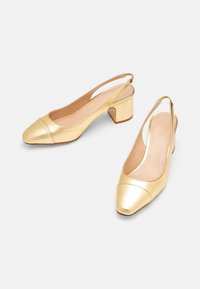 Chaussures slingback en cuir métallique doré avec des talons blocs bas et des bouts pointus sur fond blanc.