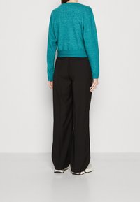 Turkos, långärmad, kort stickad tröja med en texturerad yta, tillsammans med svarta, vida byxor. Outfiten är enkel och tight.