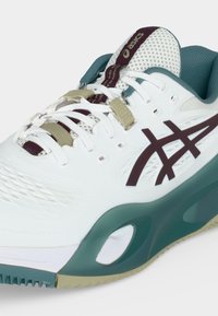 Λευκό και τιρκουάζ αθλητικό παπούτσι ASICS με σμαραγδένιο λογότυπο και μπεζ κορδόνια, με αναπνεύσιμη γλώσσα από πλέγμα και υποστηρικτικό σχεδιασμό σόλας.