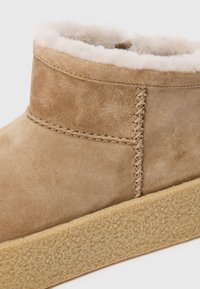 Stivale alla caviglia in suede color tan con morbida fodera in pelliccia, dettagli cuciti e suola in gomma leggera di color marrone chiaro con texture. Design semplice e minimalista.