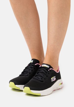 Chaussures de sport noires avec dessus en mesh, soulignées par des lacets roses et une semelle verte. Présentent le logo Skechers sur le côté et un design amorti.