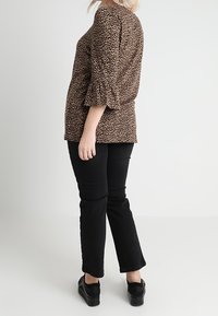 Haut à imprimé léopard marron avec manches évasées aux trois quarts, associé à un jean noir droit et des chaussures à plateforme noires. Design simple et décontracté.