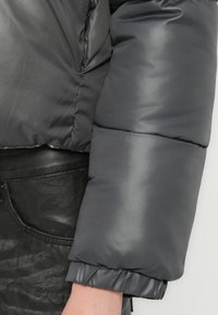 Grå pufferjakke med blank finish, elastiske mansjetter og cropped design, paret med en svart lærbukse.