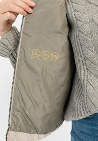 Leichte Jacke mit glattem, hellgrauem Innenleben. Verfügt über Symbole für wasserabweisende, winddichte und daunenfreie Eigenschaften. Reißverschluss.