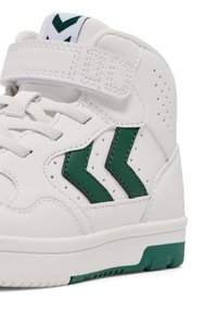 Białe sneakersy typu high-top z zielonymi akcentami, wyposażone w pasek na rzep, perforowane detale oraz kontrastującą zieloną podeszwę.