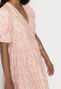 Blommönstrad rosa klänning i lätt tyg. Har en V-ringning, puffärmar och en knytning i midjan.