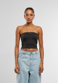 Top negru fără bretele, cu un design ajustat, textură netedă și detalii subtile ale cusăturii, purtat cu blugi din denim deschiși, cu talie înaltă.