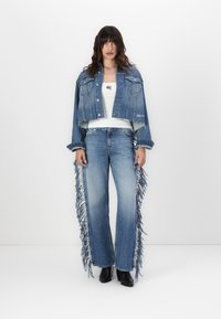 Jeansjack met een cropped ontwerp en rafelige randen, gecombineerd met wijde jeans met verticale franjes in lichtblauw. Zwarte laarzen.
