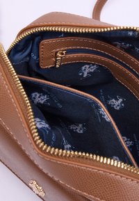 Bolso de cuero marrón texturizado con cremallera dorada, que presenta un interior forrado en azul con bolsillos y detalle de patrón.