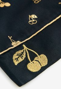 Tessuto nero con ricami in oro di ciliegie e foglie, con un dettaglio in metallo lungo il bordo, che mette in mostra cuciture e texture intricate.