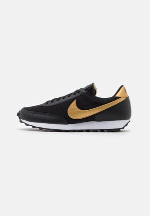 Baskets de sport noires avec le swoosh Nike doré et un détail au talon, semelle intermédiaire blanche et semelle extérieure noire texturée sur fond blanc.