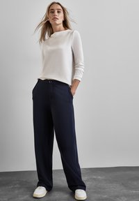 Camiseta blanca de manga larga con cuello redondo, combinada con pantalones de pierna ancha en color marino que cuentan con bolsillos y un detalle de botón. Zapatillas blancas completan el look.