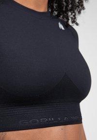 Zwarte sportbeha met een gladde stof, mesh-panelen aan de voorkant en een gestructureerde band met "GORILLA WEAR" in reliëf.