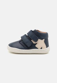 Navy Leder-Hochschaftschuh mit zwei Klettverschlüssen, weißer Sohle und strukturiertem beigen Sternakzent an der Seite. Entworfen für Komfort und Unterstützung.