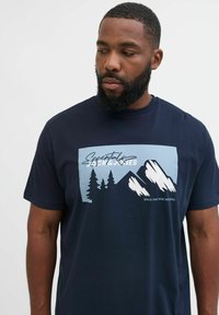 Navyblaue Baumwoll-T-Shirt mit einem grafischen Design von Bergen und Bäumen in Hellblau und Weiß, mit Text darunter. Kurze Ärmel.