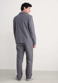 Conjunto de pijama de algodón en patrón de cuadros en azul, rojo y blanco. Cuenta con una camisa de botones y pantalones a juego con un corte relajado y mangas largas.