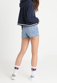Marinblå cropped hoodie med vit kant, ljusblå slitna denimshorts, vita sneakers och knälånga strumpor med rosa och marinblå ränder.