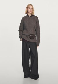 Grå strikket sweater med ribbet tekstur, parret med løse, mørke bukser. En brun læderbæltetaske bæres om livet.