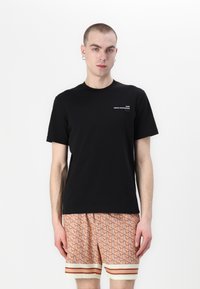 Czarna bawełniana koszulka z krótkim rękawem i okrągłym dekoltem, z białym napisem. W połączeniu z wzorzystymi szortami w kolorze brzoskwiniowym i paskowanym wykończeniem.