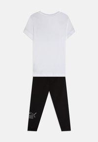 Camiseta blanca de manga corta con cuello redondo combinada con leggings negros que presentan un logo blanco en el tobillo. Tela de algodón suave.