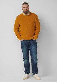 Musztardowo-żółty prążkowany sweter, dżinsowe spodnie i białe trampki. Prosty, teksturowany wzór z okrągłym dekoltem i luźnym krojem.