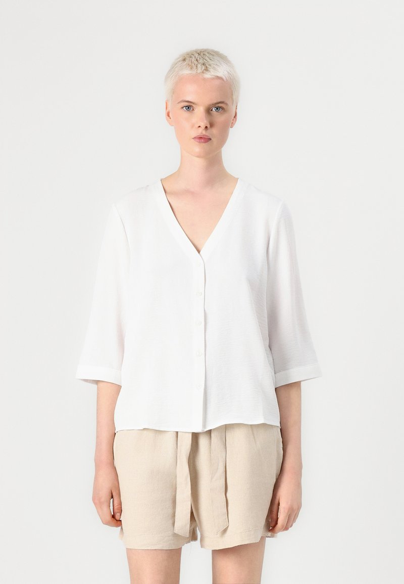 White button-up shirt with a V-neck and 3/4 sleeves, made from lightweight fabric. Paired with beige linen shorts.
