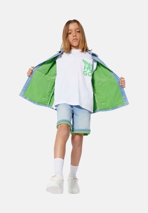 Chaqueta de mezclilla con forro verde, camiseta blanca con estampado verde, pantalones cortos azul claro con puños verdes y zapatillas blancas con logo.