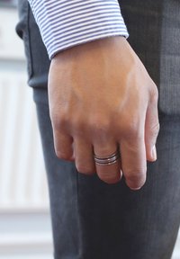Metal rings stacked on a hand with visible veins, wearing a striped blue and white shirt. Dark fabric of trousers is partially visible.