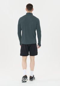 Donkergrijze langslavige shirt van vochtregulerend materiaal, gecombineerd met zwarte shorts. Model draagt witte sokken en zwarte sportschoenen.