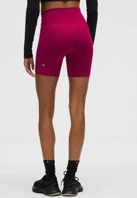 Pantalones cortos deportivos de talle alto en color fucsia, hechos de un material elástico, con una textura suave y un pequeño logo en el lateral.