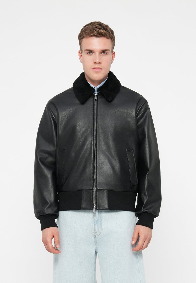 Fekete bőrbomber dzseki puha fekete prém gallérral, cipzáros záródással, bordás fekete mandzsettákkal és hempergető aljjal, valamint két oldalsó zsebbel. Simább textúra.