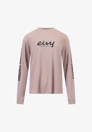 Haut à manches longues, de couleur rose pâle, en tissu côtelé. Il présente un col rond et un texte imprimé noir sur les manches et la poitrine.