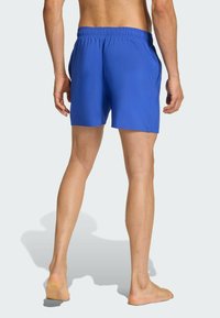 Modré plavky s elastickým pásom a bočnými vreckami, s hladkou textúrou a krátkou dĺžkou, zobrazené zozadu.