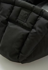 Czarna ocieplana kurtka o pikowanej strukturze, z uniesioną czarną naszywką z logo oznaczoną "EVO DIVERSE SERIES". Gładkie wykończenie materiału.