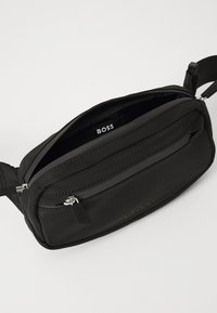 Borsa a tracolla nera in tessuto con un compartimento principale con cerniera, una tasca frontale aggiuntiva e un'etichetta BOSS all'interno. Superficie testurizzata.