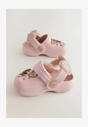 Clog-uri roz dintr-un material flexibil, cu o fundă decorativă și accente aurii pe vârf, dotate cu găuri de ventilație și curea în spate.