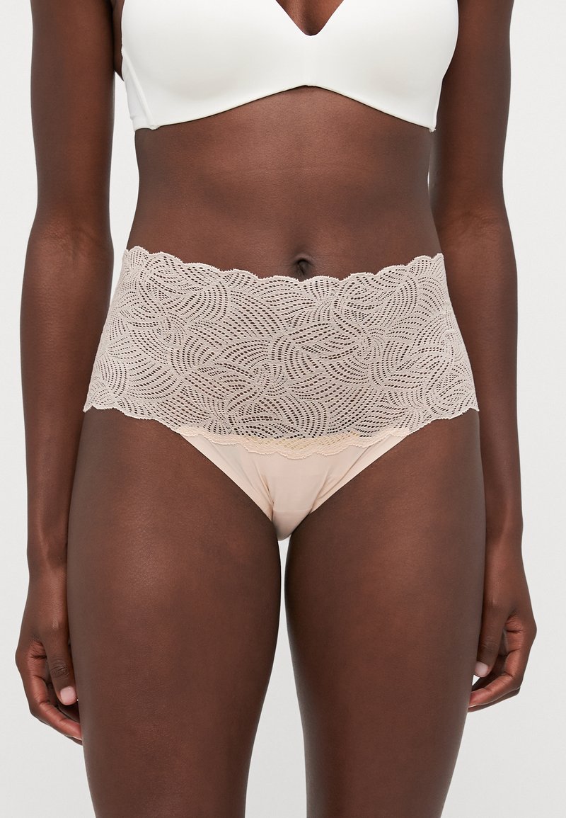 Lingerie in pizzo con una cintura ondulata color beige chiaro, caratterizzata da intricate fantasie a onde, abbinata a slip lisci color nude.