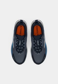 Gray athletic shoes with a reinforced toe, textured upper, blue accents, and black laces. Logo prominently displayed on the tongue.