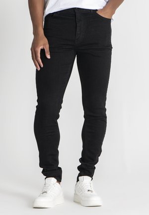 Pantalones vaqueros ajustados negros en denim elástico con cintura alta, bolsillos frontales y líneas limpias, combinados con zapatillas blancas para un look casual.