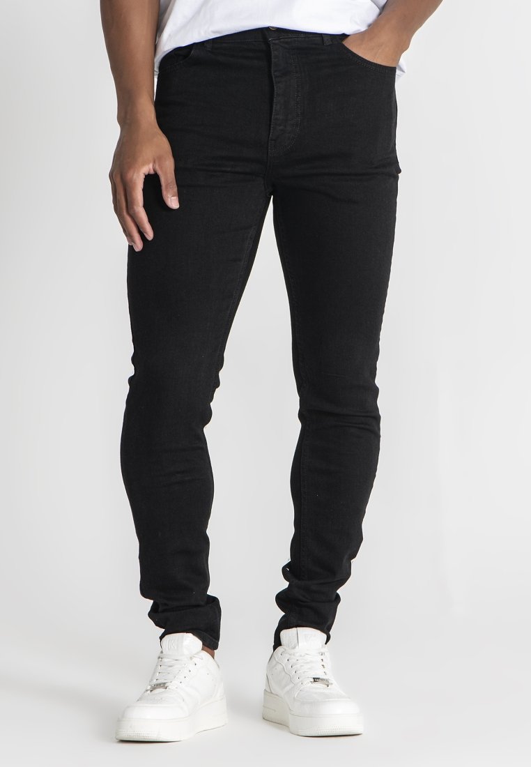 Mustat, kapeat farkut joustavasta denimmateriaalista, joissa on korkea vyötärö, etutaskut ja siistit linjat, yhdistettynä valkoisiin tennareihin rentoon ilmeeseen.