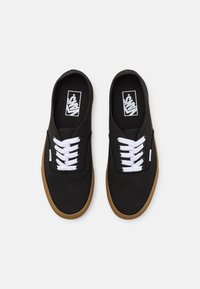 Paire de baskets Vans noires avec des lacets blancs et des semelles marron, vues de dessus sur un fond blanc.