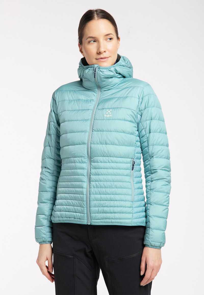 Chaqueta aislante de color azul claro con un alto cuello, diseño acolchado horizontal, cierre de cremallera en la parte delantera y bolsillos laterales. Material suave y brillante.