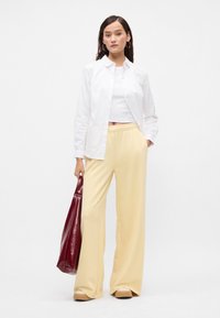 Λευκό πουκάμισο με κουμπάκια, κοντό λευκό τοπ, φαρδιά κίτρινα παντελόνια και μια λαμπερή μπορντό τσάντα. Διαθέτει επίπεδες παπούτσια με στρογγυλή μύτη.